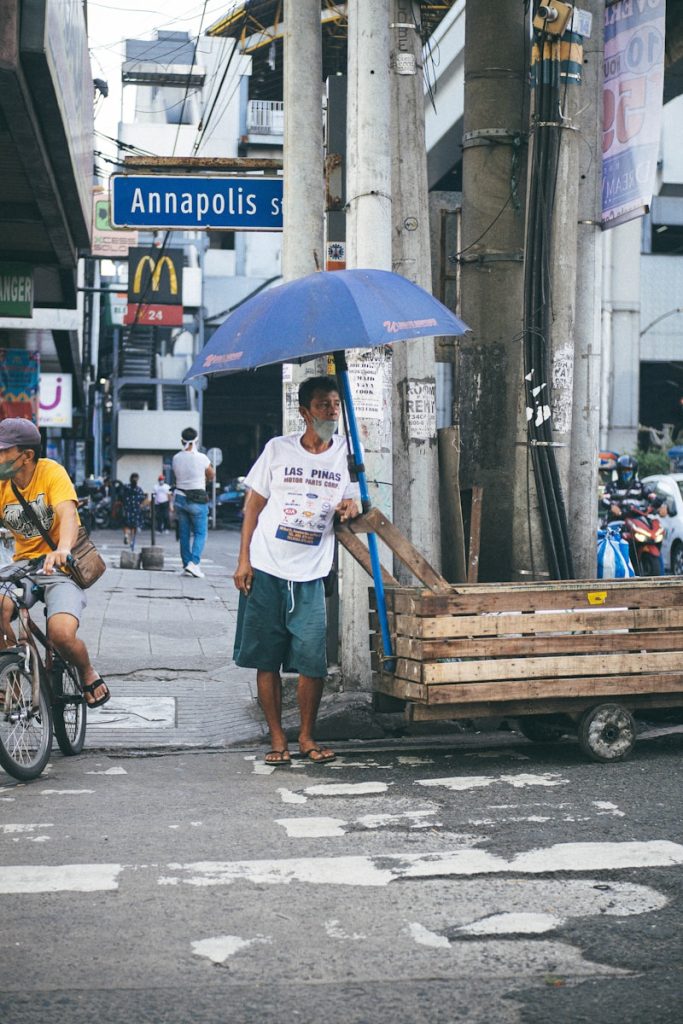 Photo by Aura Vida Lapitan a man walking down a street holding a blue umbrella