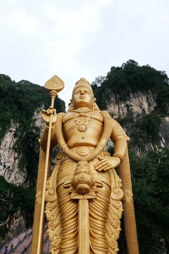 Photo by Ryan Miglinczy low angle photograph of Lord Murugan state near mountain cliff under cloudy sky